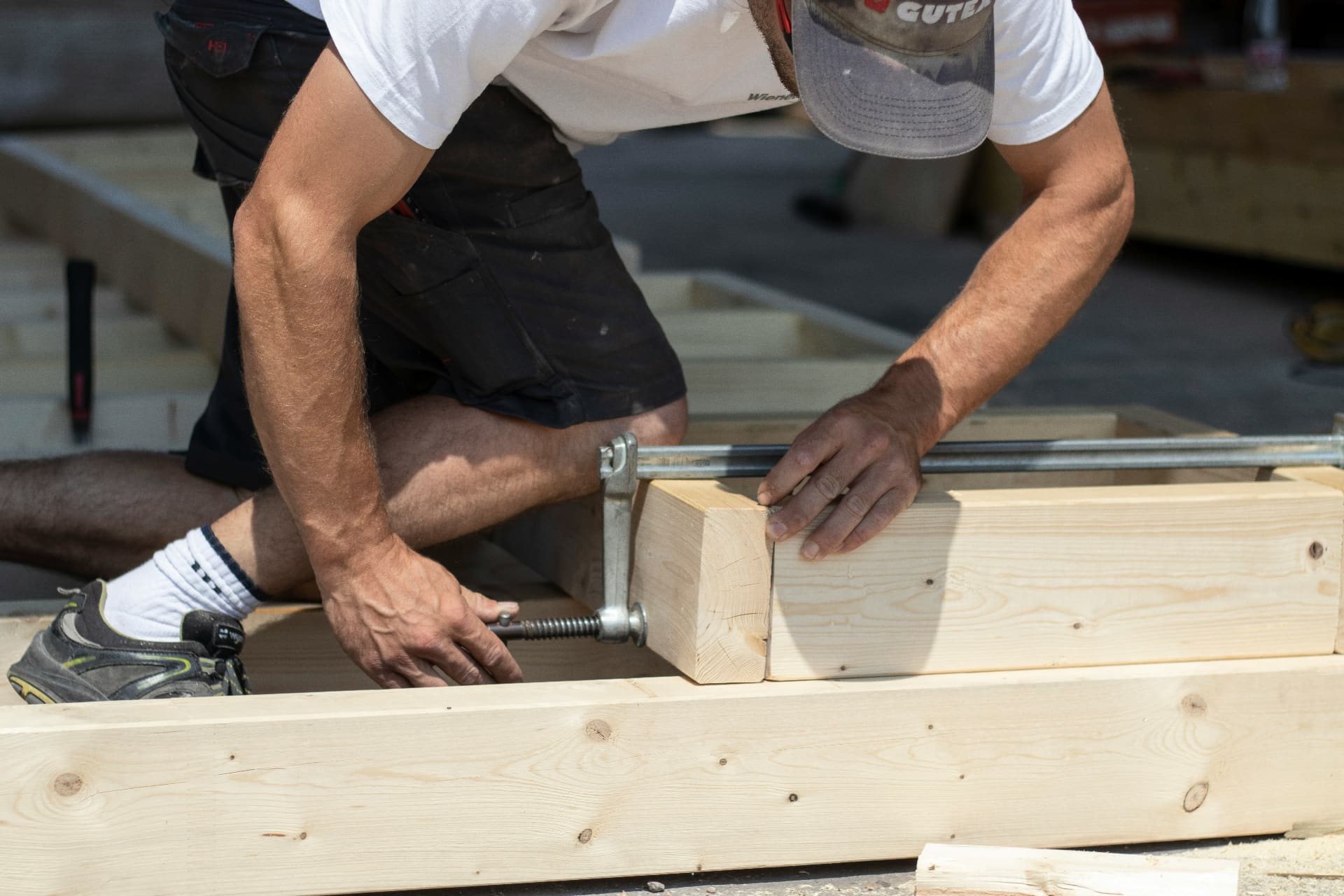Carpenter kneeling on site clamping timber beams together in bright sunlight — social media agency for carpenters and joinery businesses
