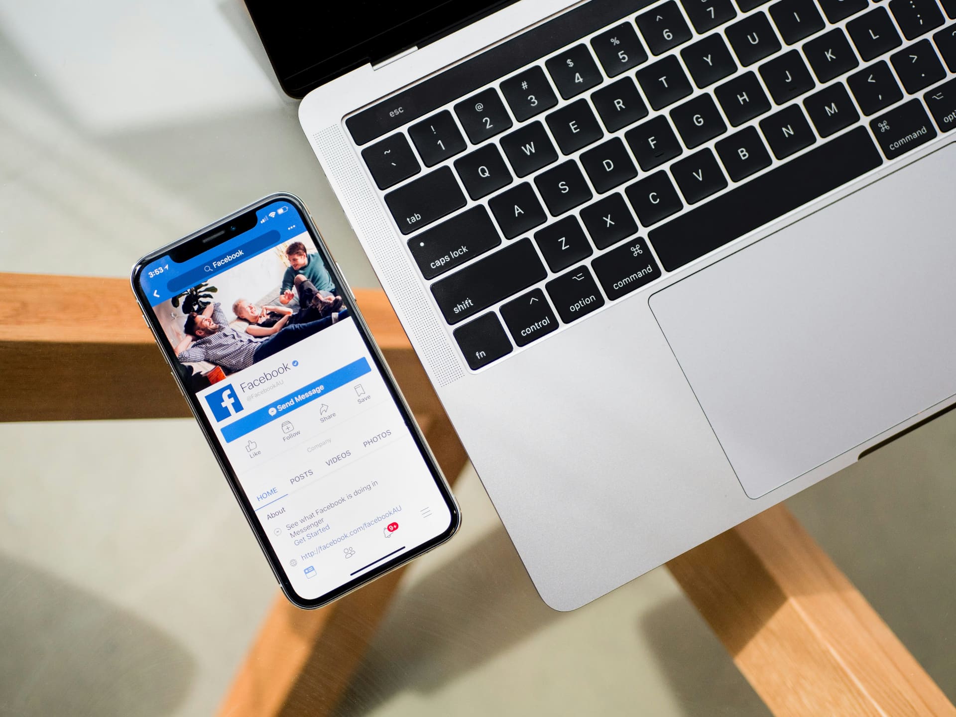 iPhone showing a Facebook page next to a MacBook keyboard on a wooden desk — Facebook marketing and page management