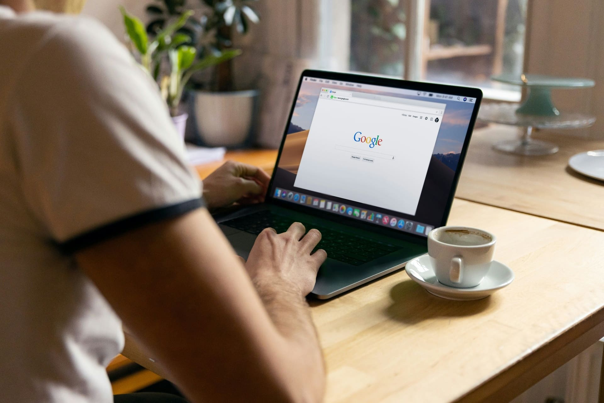 Person at a wooden desk searching on Google on a MacBook with a coffee cup beside them — Google Business Profile post and local search visibility
