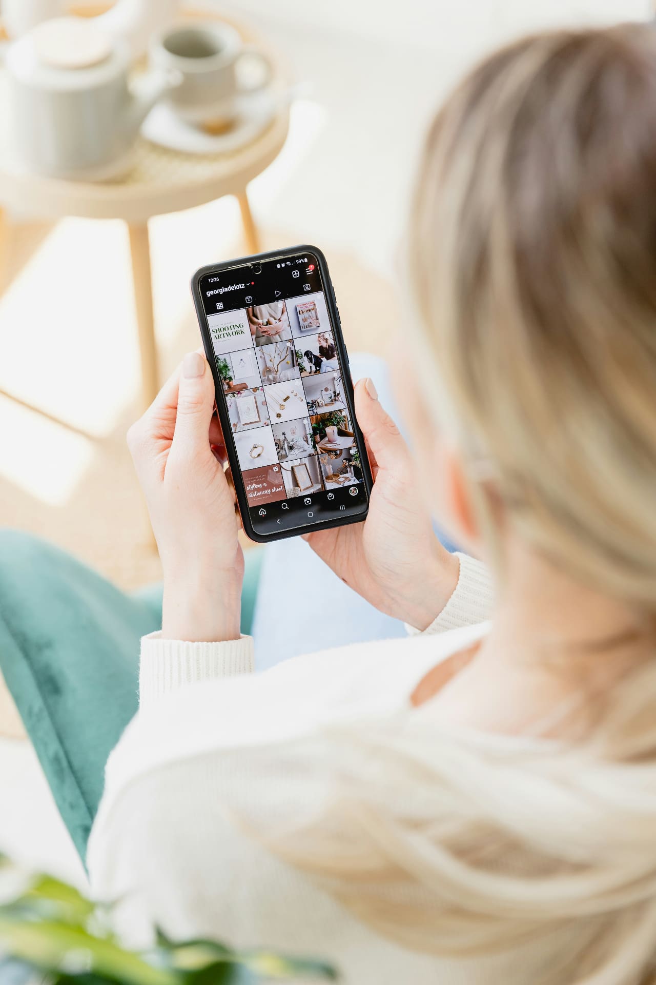 Woman holding a phone scrolling an Instagram feed grid in a softly lit room — Instagram marketing and content strategy