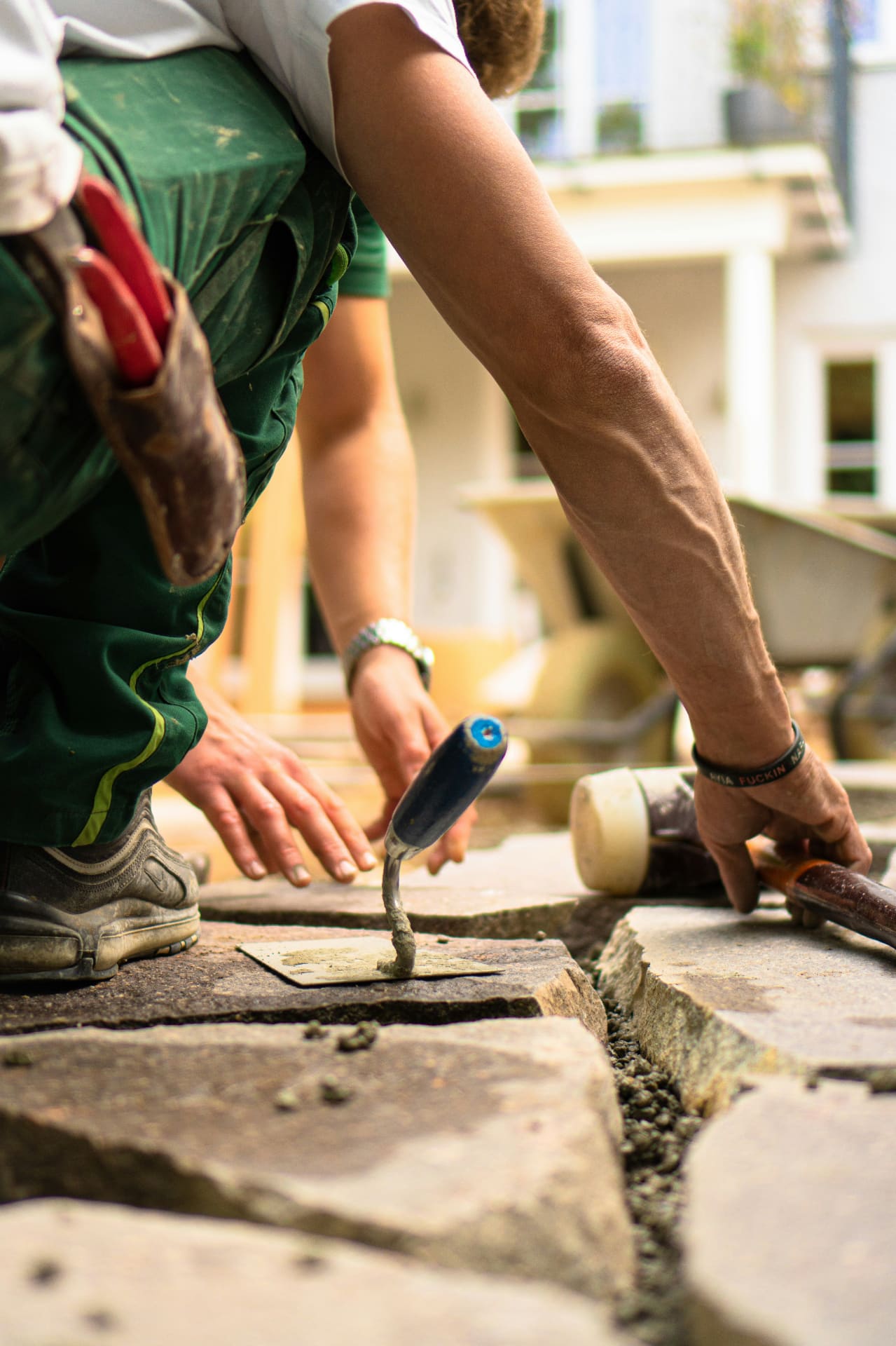 Landscaper kneeling on a garden patio pointing mortar between natural stone paving slabs with a trowel — social media agency for landscapers and garden designers