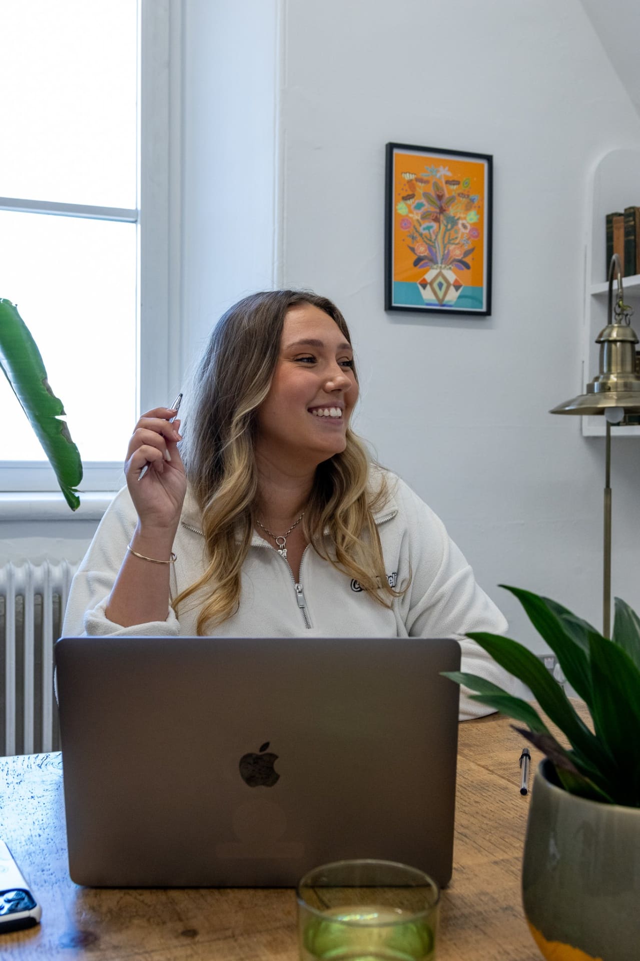 Paris Cains, Founder of Compelite Pro, smiling at her desk in a Compelite branded fleece, working on a MacBook