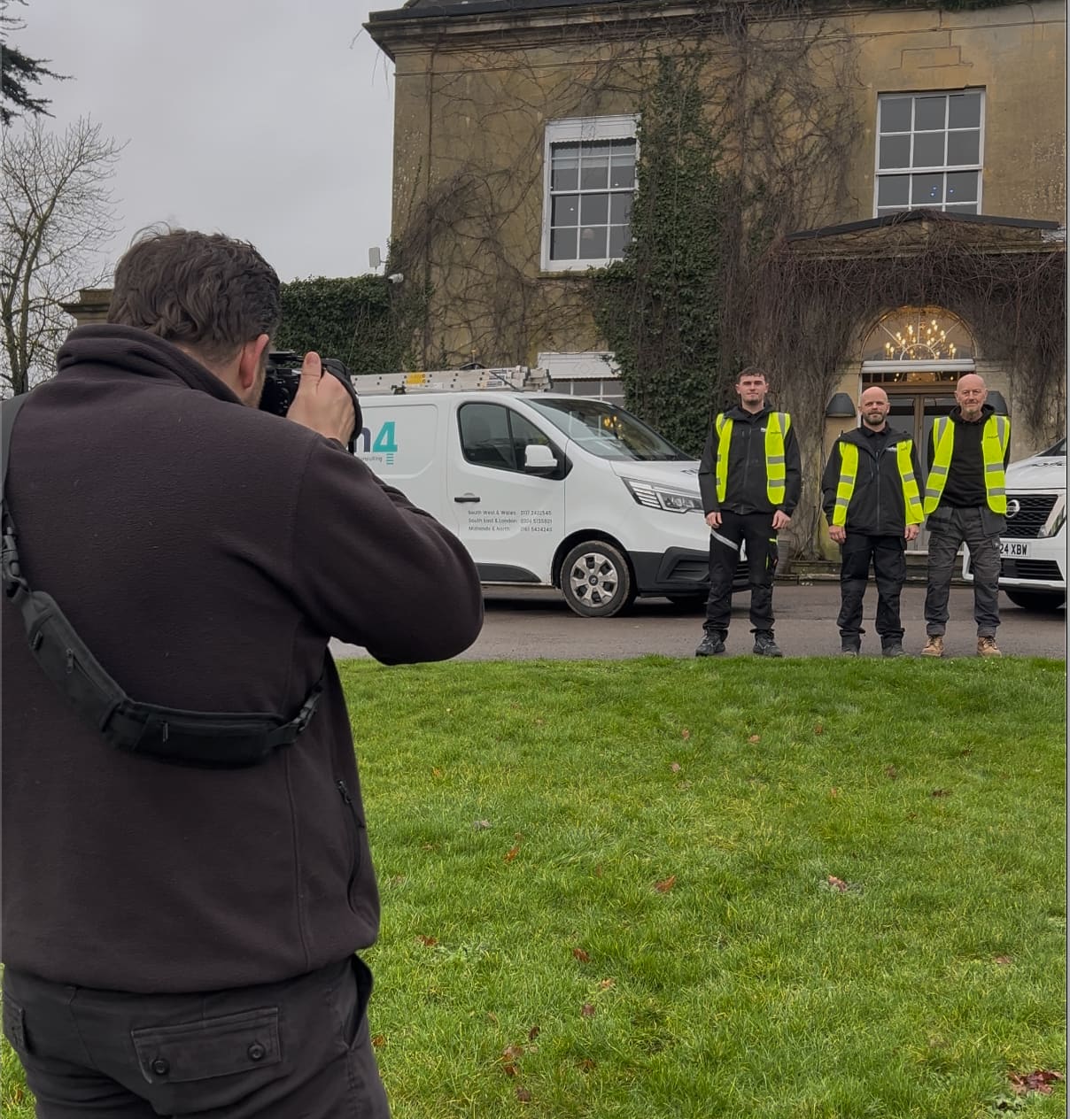 Compelite Pro photographer shooting a trades team in branded hi-vis vests beside a company van outside a Georgian manor — example trades content we'd create