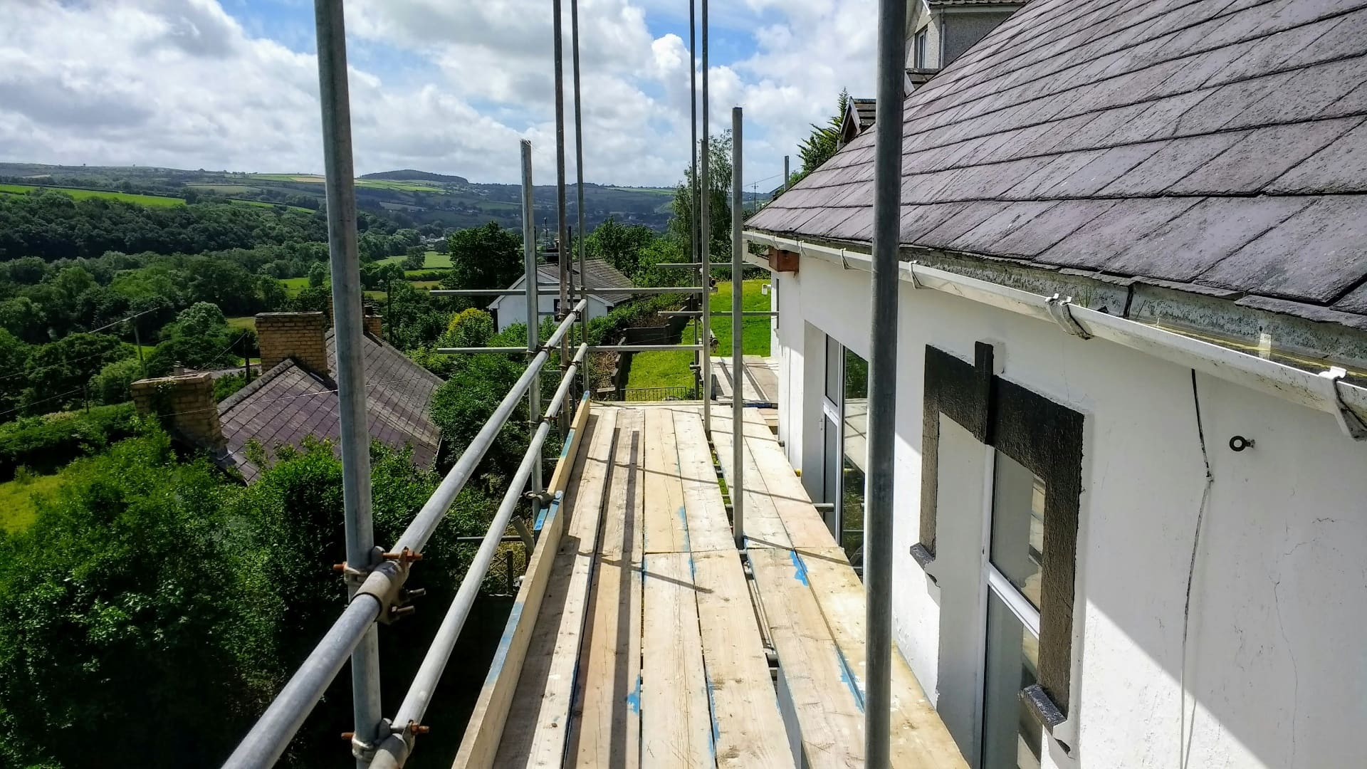 Scaffolding platform erected along the side of a rural cottage overlooking rolling green countryside — social media agency for scaffolders